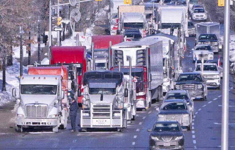 Vehicles from a Canadian protest convoy are parked blocking lanes on a road,