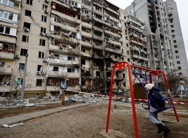 A child sits on a swing in front of a damaged residential building, after Russia launched a massive military operation against Ukraine, in Kyiv, Ukraine February 25, 2022. REUTERS/Umit Bektas