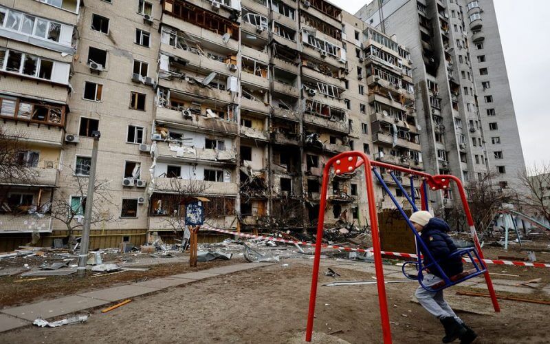 A child sits on a swing in front of a damaged residential building, after Russia launched a massive military operation against Ukraine, in Kyiv, Ukraine February 25, 2022. REUTERS/Umit Bektas