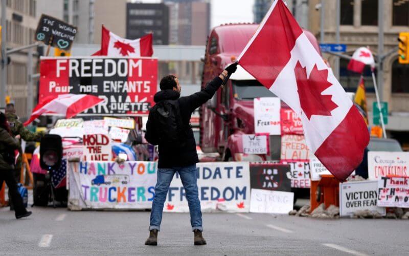 A protester waves a Canadian flag in front of parked vehicles on Rideau Street on the 15th day of a protest against COVID-19 measures that has grown into a broader anti-government protest, in Ottawa, Friday, Feb. 11, 2022. (Justin Tang/THE CANADIAN PRESS)