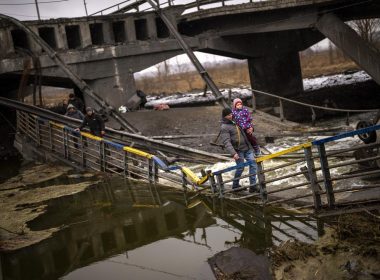 Local militiaman Valery, 37, carries a child as he helps a fleeing family across a bridge destroyed by artillery, on the outskirts of Kyiv, Ukraine, Wednesday, March 2. 2022. Russian forces have escalated their attacks on crowded cities in what Ukraine's leader called a blatant campaign of terror. (AP Photo/Emilio Morenatti)
