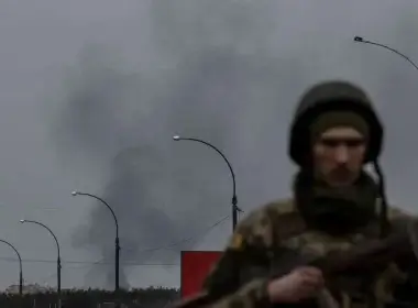 Smoke rises as a service member of the Ukrainian armed forces stands by the only escape route used by locals to evacuate from the town of Irpin, after days of heavy shelling, while Russian troops advance towards the capital, in Irpin, near Kyiv, Ukraine March 7, 2022. REUTERS/Carlos Barria