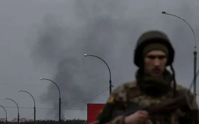 Smoke rises as a service member of the Ukrainian armed forces stands by the only escape route used by locals to evacuate from the town of Irpin, after days of heavy shelling, while Russian troops advance towards the capital, in Irpin, near Kyiv, Ukraine March 7, 2022. REUTERS/Carlos Barria