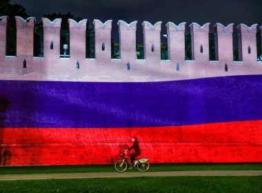 A woman rides a bicycle past a part of the Kremlin wall where the Russian national flag is projected, during celebrations of Russia Day in Moscow, Russia, June 12, 2020. REUTERS/Maxim Shemetov/File Photo