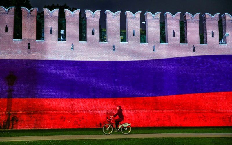 A woman rides a bicycle past a part of the Kremlin wall where the Russian national flag is projected, during celebrations of Russia Day in Moscow, Russia, June 12, 2020. REUTERS/Maxim Shemetov/File Photo