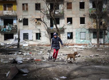 A man walks with his dog near an apartment building damaged by shelling from fighting on the outskirts of Mariupol, Ukraine, in territory under control of the separatist government of the Donetsk People's Republic, on Tuesday, March 29, 2022. (AP Photo/Alexei Alexandrov)