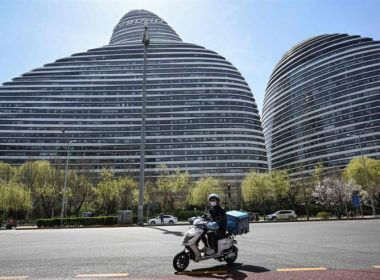 A food delivery worker rides a scooter past an office compound where recent COVID-19 cases have been detected in Beijing, Thursday. AFP-Yonhap