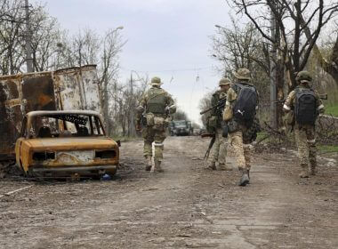 Servicemen of Donetsk People's Republic militia walk past damaged vehicles during a heavy fighting in an area controlled by Russian-backed separatist forces in Mariupol, Ukraine, Tuesday, April 19, 2022. Taking Mariupol would deprive Ukraine of a vital port and complete a land bridge between Russia and the Crimean Peninsula, seized from Ukraine from 2014. (AP Photo/Alexei Alexandrov)