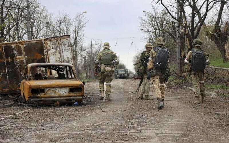 Servicemen of Donetsk People's Republic militia walk past damaged vehicles during a heavy fighting in an area controlled by Russian-backed separatist forces in Mariupol, Ukraine, Tuesday, April 19, 2022. Taking Mariupol would deprive Ukraine of a vital port and complete a land bridge between Russia and the Crimean Peninsula, seized from Ukraine from 2014. (AP Photo/Alexei Alexandrov)