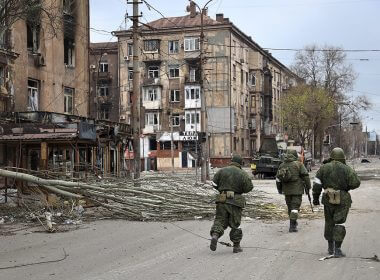 Service members of the militia from the Donetsk People's Republic walk past damaged apartment buildings in an area controlled by Russian-backed separatist forces in Mariupol, Ukraine, on April 16. | Alexei Alexandrov/AP Photo