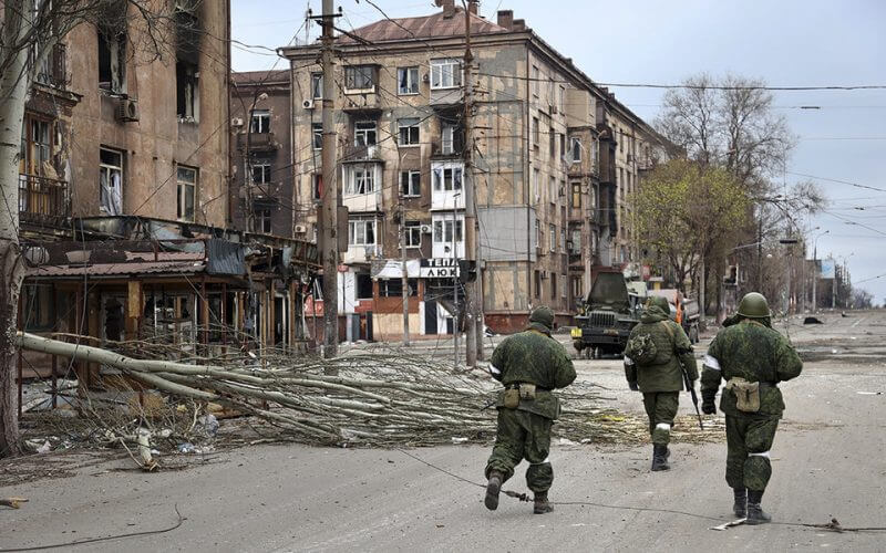 Service members of the militia from the Donetsk People's Republic walk past damaged apartment buildings in an area controlled by Russian-backed separatist forces in Mariupol, Ukraine, on April 16. | Alexei Alexandrov/AP Photo