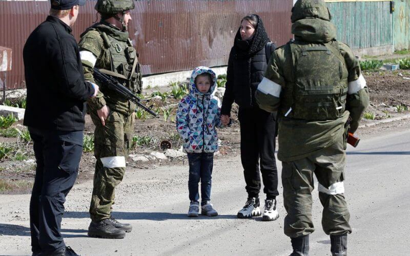 A woman with a child talks to service members of pro-Russian troops as evacuees board buses to leave the city during Ukraine-Russia conflict in the southern port of Mariupol, Ukraine April 20, 2022. REUTERS/Alexander Ermochenko
