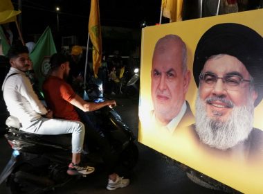 Supporters carry Hezbollah and Amal Movement flags as they ride in a convoy past a poster depicting Hezbollah leader Sayyed Hassan Nasrallah and Head of Hezbollah's parliamentary bloc Mohamed Raad, as votes are being counted in Lebanon's parliamentary election, in Nabatiyeh, southern Lebanon May 15, 2022. REUTERS/Issam Abdallah