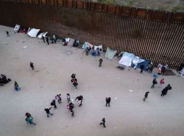 In an aerial view, migrants gather along the U.S. border wall from Mexico on Dec. 10, 2021 in Yuma, Ariz. | John Moore/Getty Images