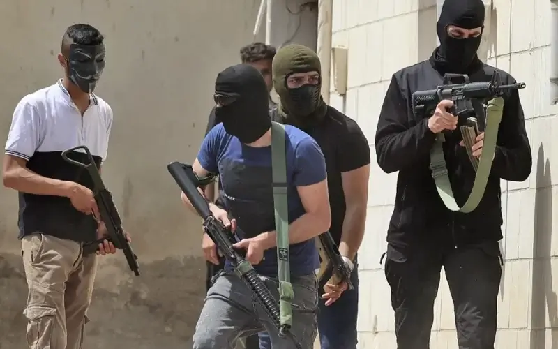 Masked Palestinian men hold automatic weapons during clashes with Israeli security forces in the West Bank city of Jenin on May 13, 2022. JAAFAR ASHTIYEH / AFP