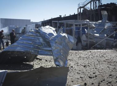 People stand near a destroyed building on the outskirts of Odesa, Ukraine, Tuesday, May 10, 2022. The Ukrainian military said Russian forces fired seven missiles a day earlier from the air at the crucial Black Sea port of Odesa, hitting a shopping center and a warehouse. (AP Photo/Max Pshybyshevsky)