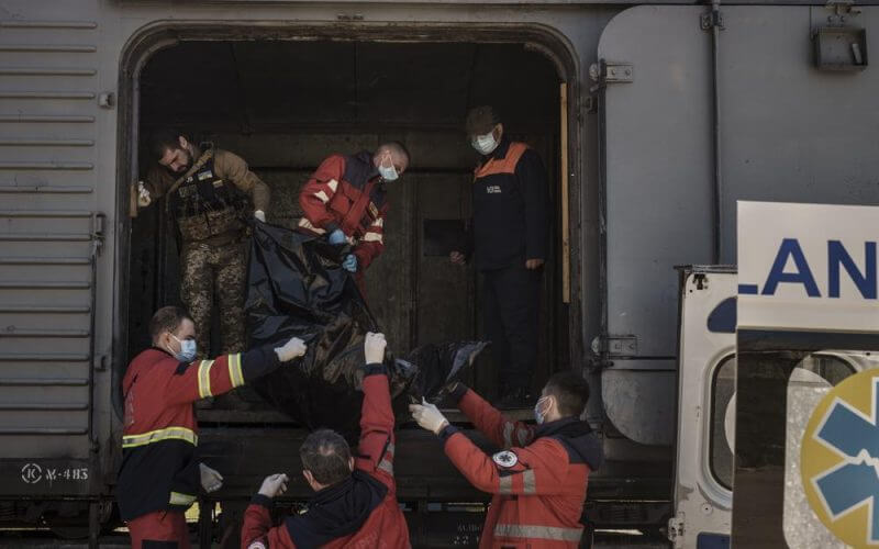 A Ukrainian serviceman and emergency workers carry the body of a Russian soldier into a refrigerated train in Kharkiv, Ukraine, Thursday, May 5, 2022. The bodies of more than 40 Russian soldiers who were found after battles around Kharkiv are being stored in the refrigerated car. (AP Photo/Felipe Dana)