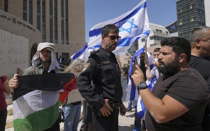 Supporters of Mohammed el-Halabi hold a Palestinian flag and placards as protesters wave Israeli flags, outside the district court in the southern Israeli city of Beersheba, Wednesday, June 15, 2022. (AP Photo/Tsafrir Abayov)