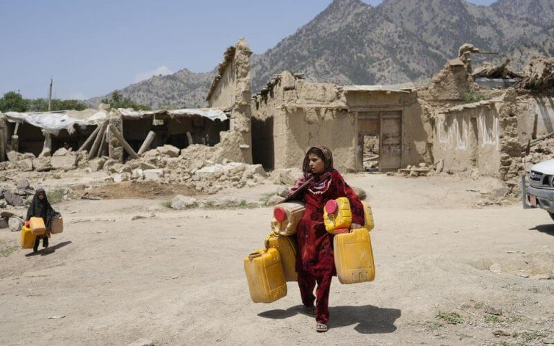 Afghan girl carries canisters in front of destroyed homes after an earthquake in Gayan district in Paktika province, Afghanistan, Sunday, June 26, 2022. (AP Photo/Ebrahim Nooroozi)