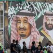 Football fans stand beneath a large banner depicting Saudi King Salman bin Abdulaziz (C) and his son Crown Prince Mohammed bin Salman (R) as they attend the World Cup 2022 Asian qualifying match between Palestine and Saudi Arabia in the town of al-Ram in the West Bank on October 15, 2019. (Ahmad GHARABLI / AFP / File)