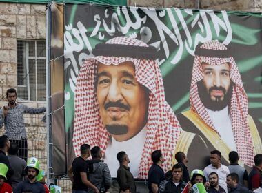 Football fans stand beneath a large banner depicting Saudi King Salman bin Abdulaziz (C) and his son Crown Prince Mohammed bin Salman (R) as they attend the World Cup 2022 Asian qualifying match between Palestine and Saudi Arabia in the town of al-Ram in the West Bank on October 15, 2019. (Ahmad GHARABLI / AFP / File)