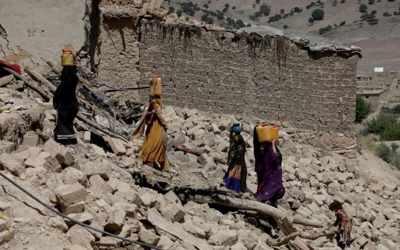 Afghan women carry water containers through the debris of damaged houses after the recent earthquake in Wor Kali village in the Barmal district of Paktika province, Afghanistan, June 25, 2022. REUTERS/Ali Khar