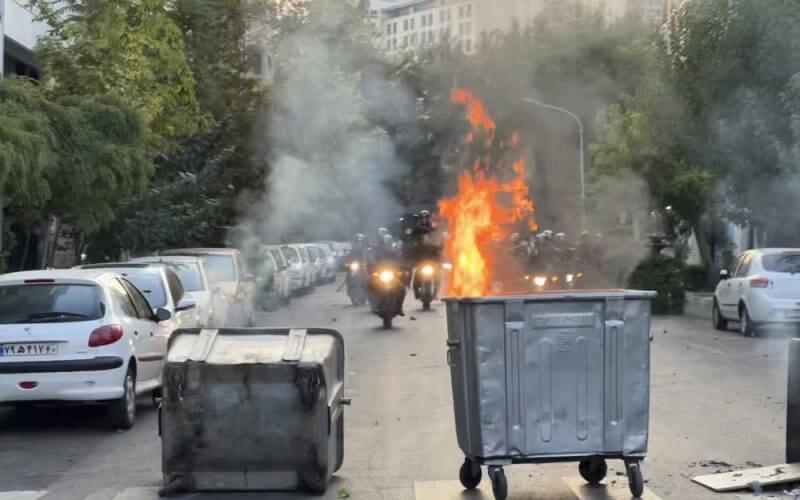In this Tuesday, Sept. 20, 2022, photo taken by an individual not employed by the Associated Press and obtained by the AP outside Iran, a trash bin is burning as anti-riot police arrive during a protest over the death of a young woman who had been detained for violating the country's conservative dress code, in downtown Tehran, Iran. AP