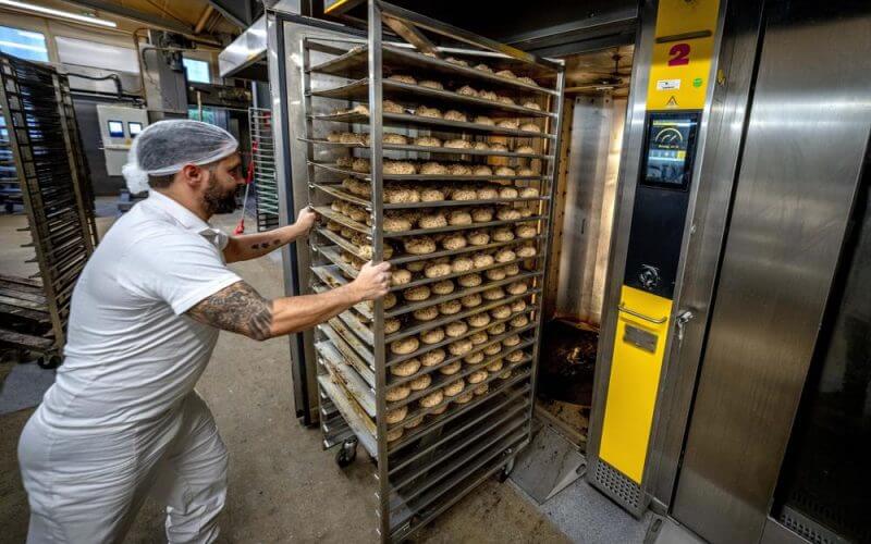 An employee pushes bread rolls into one of the gas heated ovens in the producing facility in Cafe Ernst in Neu Isenburg, Germany, Monday, Sept. 19, 2022. AP
