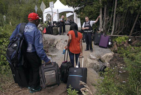 In this Aug. 7, 2017 file photo, a Royal Canadian Mounted Police officer informs a migrant couple of the location of a legal border station, shortly before they illegally crossed from Champlain, N.Y., to Saint-Bernard-de-Lacolle, Quebec. AP