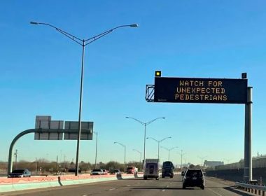 An electronic sign flashes "Watch for unexpected pedestrians," Tuesday, Dec. 20, 2022, on the highway next to the fenced US-Mexican border just east of downtown El Paso, Texas, next to one of the three bridges that connect the Texas city with the sprawling metropolis of Juarez, Mexico. AP