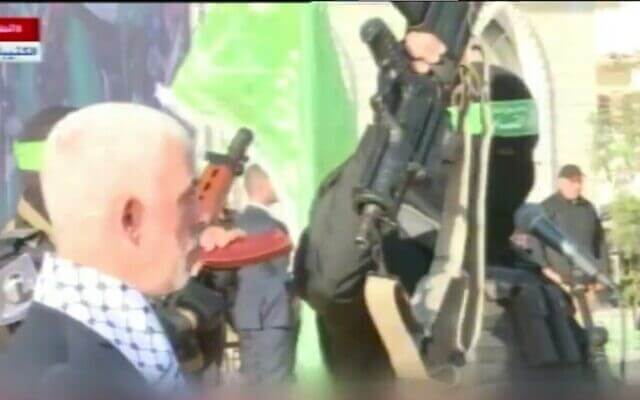 A masked member of Hamas holds up the supposed weapon of slain Israeli soldier Hadar Goldin, as the terror group's Gaza leader Yahya Sinwar looks on during a rally, December 14, 2022. (Video screenshot)