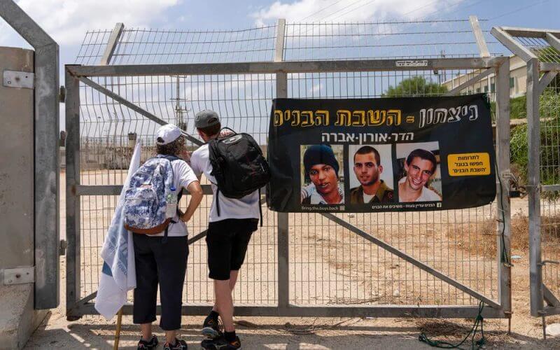 Israelis look towards the fence for the Erez border crossing on the Israel-Gaza border, next to a banner showing captive Israeli civilians Avera Mengistu (L) and late soldiers Oron Shaul (C) and Hadar Goldin. AP