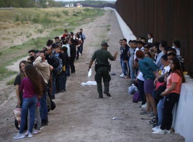A group of migrants stand next to the border wall as a Border Patrol agent takes a head count in Eagle Pass, Texas, Saturday, May 21, 2022. AP