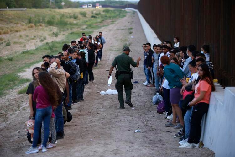 A group of migrants stand next to the border wall as a Border Patrol agent takes a head count in Eagle Pass, Texas, Saturday, May 21, 2022. AP