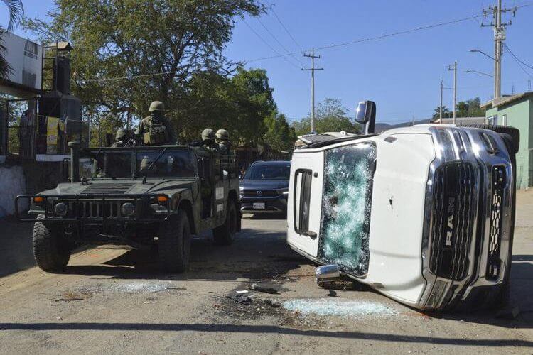 Army soldiers drive past a destroyed vehicle on the streets of Jesus Maria, Mexico, on Saturday, Jan. 7, 2023, the small town where Ovidio Guzman was detained earlier in the week. Martin Urista / AP