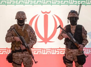 Two Islamic Revolutionary Guard Corps (IRGC) armed military personnel pose for a photograph in front of an Iran flag during a pro-government protest rally in southern Tehran, December 29, 2022. (Morteza Nikoubazl/NurPhoto via Getty Images)