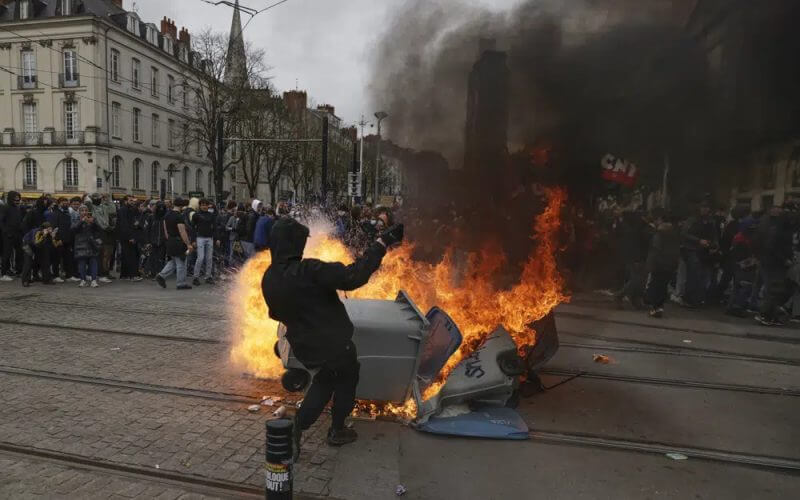 A protester stands next to a burning waste container during a rally in Nantes, western France, Thursday, march 23, 2023. AP