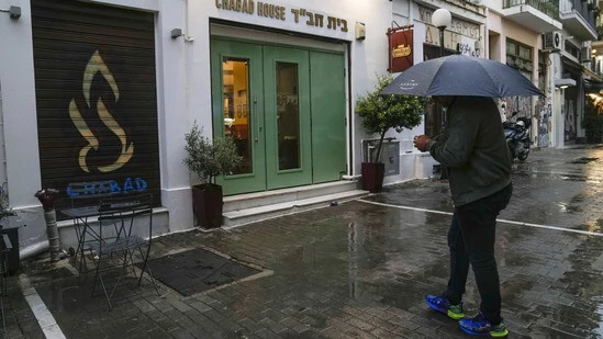A man holding an umbrella stands in front of a Jewish restaurant that Greek officials believe was one of the targets of a planned terrorist attack, in central Athens. AP
