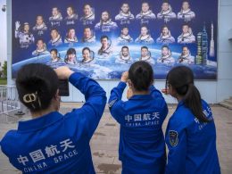 Staff members take photos of a billboard depicting Chinese astronauts at the Jiuquan Satellite Launch Center in northwest China on Monday, May 29, 2023. (AP Photo/Mark Schiefelbein)