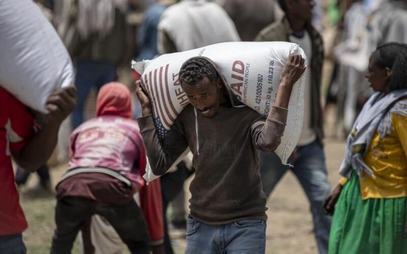 An Ethiopian man carries a sack of wheat on his shoulders to be distributed by the Relief Society of Tigray in the town of Agula, in the Tigray region of northern Ethiopia, on Saturday, May 8, 2021. (AP Photo/Ben Curtis)