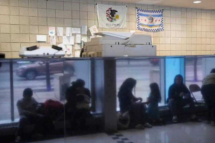 Immigrants from Venezuela are reflected in a marble wall while taking shelter at the Chicago Police Department's 16th District station on Monday, May 1, 2023. Charles Rex Arbogast | AP
