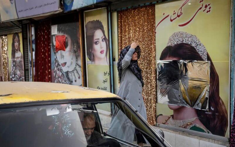 A woman walks past beauty salons with window decorations which have been defaced in Kabul, Afghanistan, Sunday, Sept. 12, 2021. (AP Photo/Bernat Armangue, File)