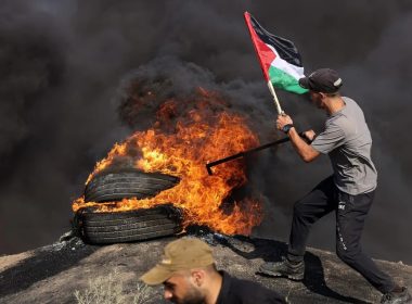 A Palestinian youth holds a flag next to burning tyres during a protest by the border fence with Israel east of Gaza City. MAHMUD HAMS / AFP