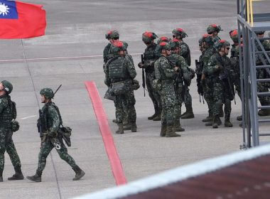 A Taiwanese soldier holds a Taiwan national flag near a group of soldiers with red markings on their helmets to play the role of an enemy during the annual Han Kuang military exercises simulating an attack on an airfield at Taoyuan International Airport in Taoyuan, Northern Taiwan, July 26, 2023. (AP Photo/Chiang Ying-ying, File)