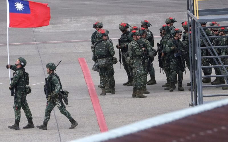 A Taiwanese soldier holds a Taiwan national flag near a group of soldiers with red markings on their helmets to play the role of an enemy during the annual Han Kuang military exercises simulating an attack on an airfield at Taoyuan International Airport in Taoyuan, Northern Taiwan, July 26, 2023. (AP Photo/Chiang Ying-ying, File)