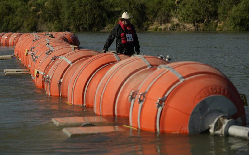 A kayaker walks past large buoys being used as a floating border barrier on the Rio Grande, Aug. 1, 2023, in Eagle Pass, Texas. (AP Photo/Eric Gay, File)