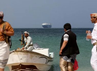 Armed men stand on the beach as the Galaxy Leader commercial ship, seized by Yemen’s Houthis last month, is anchored off the coast of al-Salif, Yemen, December 5, 2023. REUTERS