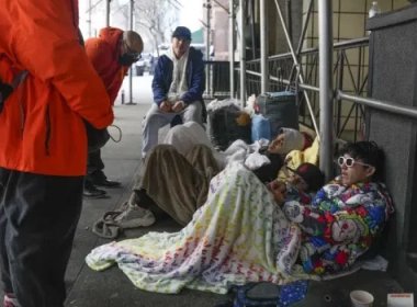 Recent illegal immigrants to the United States lie on the sidewalk with their belongings as they talk to city officials in front of the Watson Hotel in New York. AP