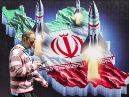 A man walks past a banner depicting missiles launching from a representation of the map of Iran colored with the Iranian flag in central Tehran on April 15, 2024. (ATTA KENARE / AFP)